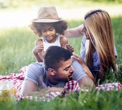 image of a family; mother and father laying on the grass with their baby overjoyed with their new Univeral Life Insurance Policy from the best insurance agency in Bartlett, TN